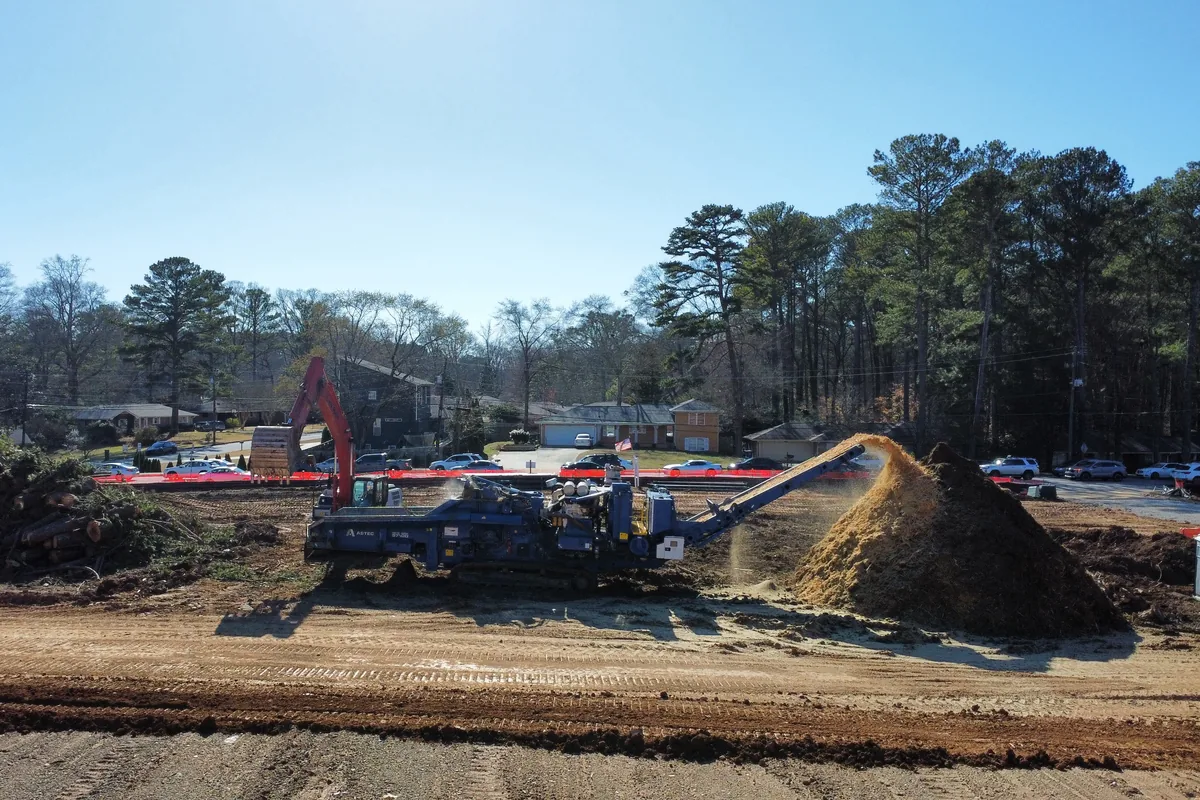 Horizontal grinder discharging a pile of wood mulch on a cleared Georgia site with an excavator feeding it