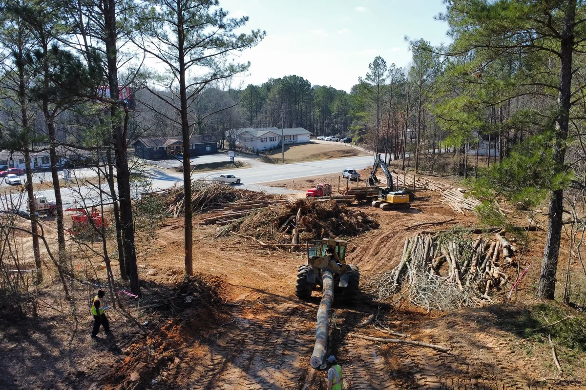 Land clearing site in Georgia with stacked logs, brush piles, a horizontal grinder, and a loader beside a road